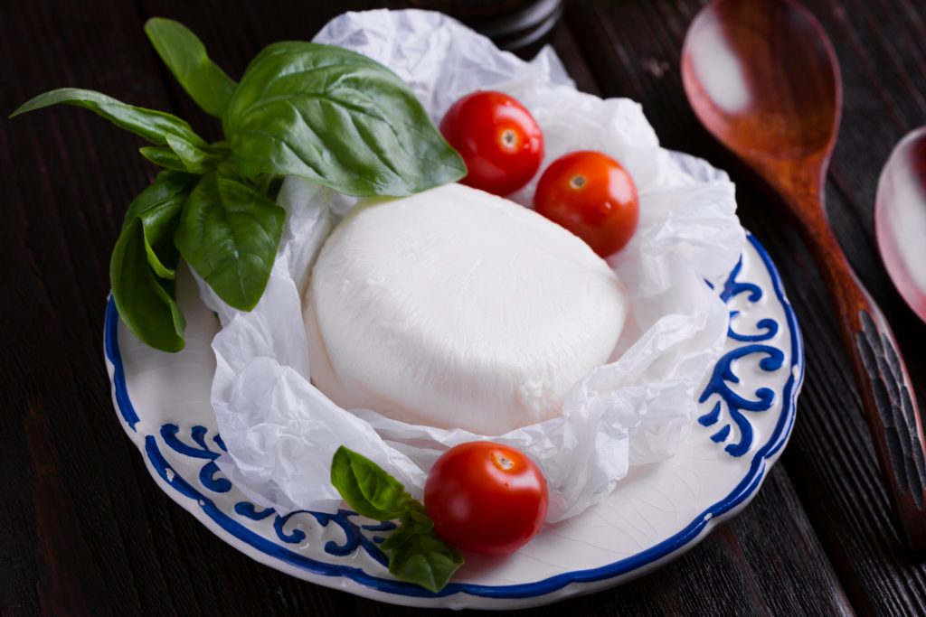 La Burrata es un queso fresco de leche de vaca originario de la región italiana de Apulia, específicamente de la ciudad de Ándria. Su nombre deriva de la palabra italiana «burro», que significa mantequilla, haciendo referencia a su textura cremosa y untuosa. La Burrata tiene la apariencia externa de una bolsa de mozzarella, pero al cortarla, su interior está compuesto por una mezcla de queso fresco y crema conocida como stracciatella. Esta combinación le da una textura muy suave y un sabor delicado que la distingue de otros quesos frescos. Uso Culinario: Es común utilizar la Burrata en ensaladas, acompañada de tomates frescos y un buen aceite de oliva. También puede servirse sobre tostadas o buen pan, realzando su sabor y textura. En resumen, la Burrata es un queso italiano fresco y cremoso con una rica historia y una textura única que se disfruta en diversas preparaciones culinarias.